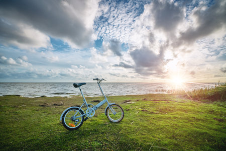 Foldable bike by the ocean at sunset. Active in nature by the sea watching the sunset. Blue bicycle standing near water in a beautiful landscapeの写真素材