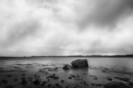 Large rock in the silky smooth water by the shore in monochrome tone
