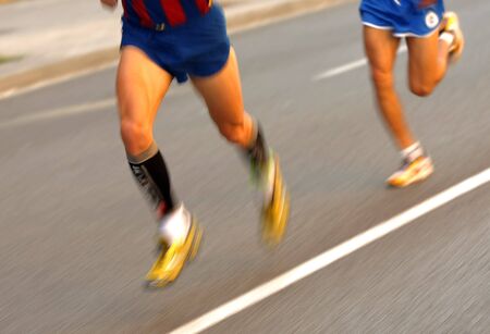 Marathon runner legs on the road followed by another runner with panning blurの写真素材