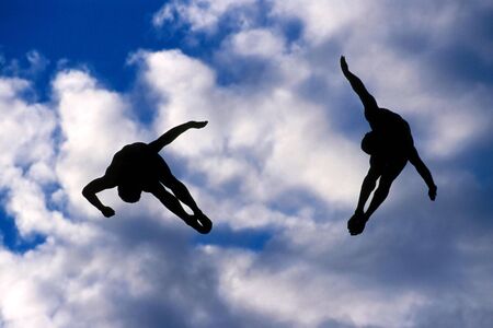 A pair of synchronized divers silhouetted in the sky.の写真素材