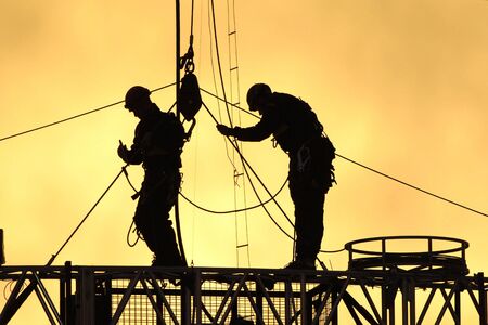 Two workers climb to fix the lines at stadium in the sunset.の写真素材