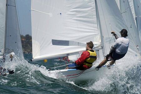 Two sailors hang off the side of the boat.