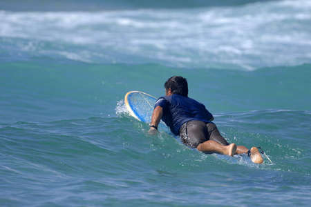 A lone surfer paddles out through the surf and waves.