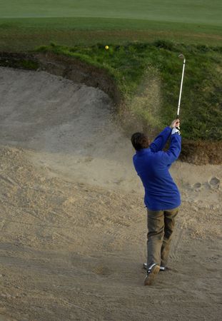 A left handed golfer blast out of a deep sand trap.の写真素材