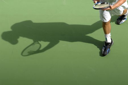 The shadow of a male tennis player walks back to serve during a match.の写真素材