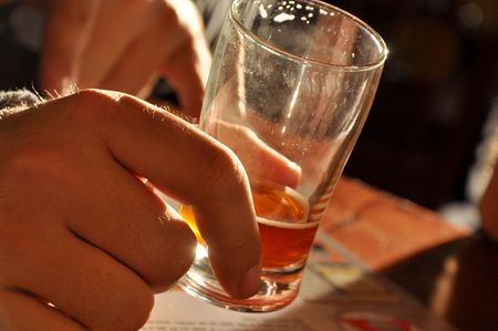 A male holds a near empty beer in a bar in the afternoon light.