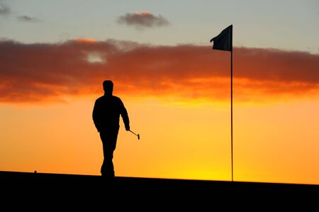 a male golfer goes to remove the flag before he putts at sunriseの写真素材