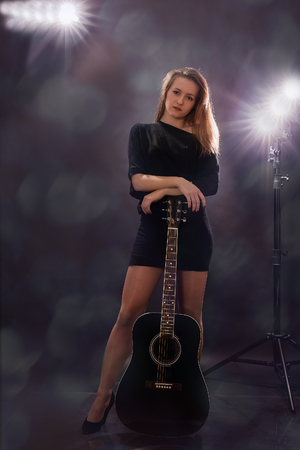 Beautiful girl with guitar on black background.の写真素材