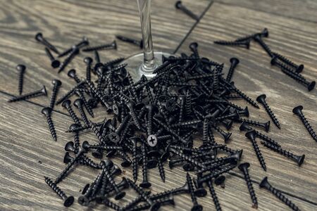 Pile of black screw nails on wooden background. Lots of screws on the table.