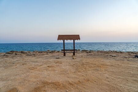Romantic wooden bench overlooking the beautiful azure lagoon at sunset near Cape Greco. Cyprus.の写真素材
