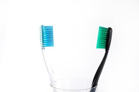Toothbrushes of different colors in a glass beaker on a white background.