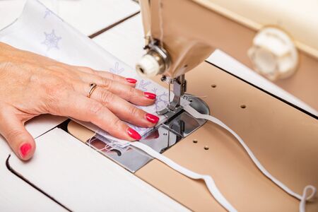 Girl sews masks to protect against the corona virus. Woman hands using the sewing machine to sew the...