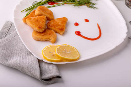 On the table on a white plate, chicken nuggets with lemon. In the background, different seasonings. The smile is drawn with spicy sauce. The concept of fast food.の写真素材