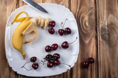 A half-peeled banana was cut into slices on a white plate. Dessert.