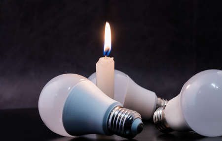 Three light bulbs and one candle on a black background.の写真素材