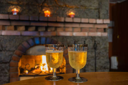 Two plastic glasses with cold champagne on the background of a burning fireplace.の写真素材