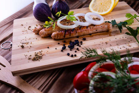 Grilled sausages with seasonings and herbs on a cutting Board. Onion rings and lemon.