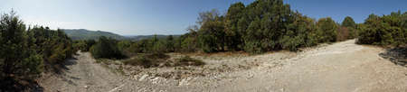 Panorama with a view of a dirt road and mountains in the background on a Sunny warm day.