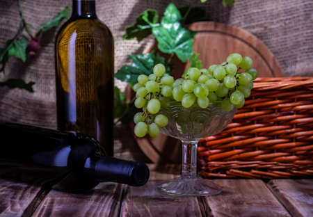 Two bottles of red and white wine on a wooden table with a bunch of grapes. Selective focus.の写真素材