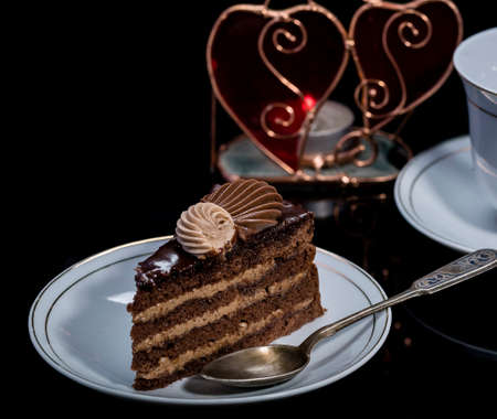 A piece of chocolate cake on a saucer on a black background. Delicious breakfast.Traditional...