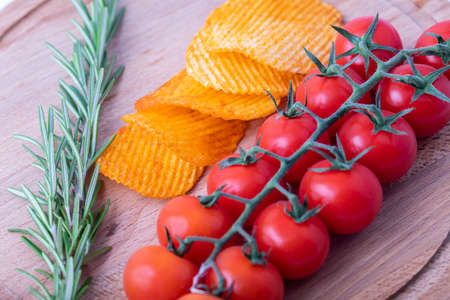 Potato chips with a sprig of rosemary and cherry tomatoes on a wooden table. Cherrytomatoeson a branch.の写真素材