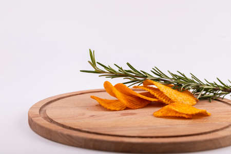 Potato chips with a sprig of rosemary in a glass bowl on a wooden table. A few slices are on the...