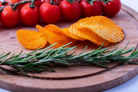 Potato chips with a sprig of rosemary and cherry tomatoes on a wooden table. Cherrytomatoeson a...
