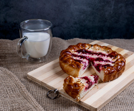 Pie with cherries and cottage cheese on a wooden Board cut off a piece and a Cup of milk on the background of burlap.の写真素材