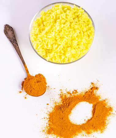 A spoon with turmeric and a plate of rice on a white background.の写真素材