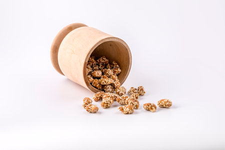 Cashew nuts in sesame seeds spilled out of a wooden bowl on the white table.の写真素材