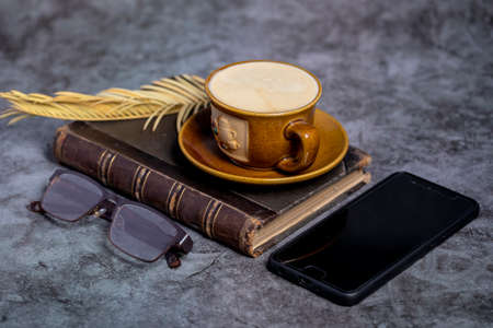A cup of coffee, an old book, glasses, and a phone on the table.の写真素材