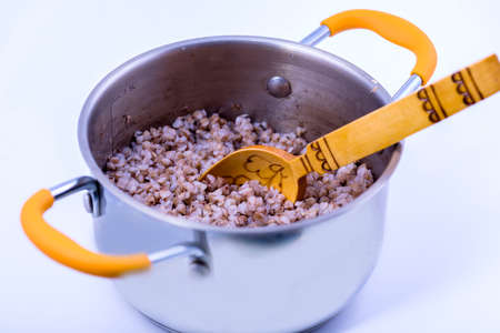 Buckwheat porridge in a saucepan with a wooden spoon on a white background.の写真素材