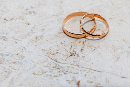 Two yellow gold rings are lying on a stone-textured table.の写真素材