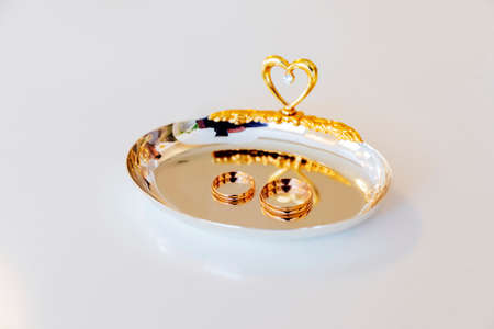 Wedding gold rings are lying on a yellow plate with a heart for a wedding.の写真素材