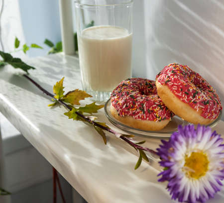 Fresh donuts and a glass of milk for breakfast, a beautiful summer flower and a good mood.の写真素材