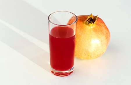 A pomegranate and a glass glass with pomegranate juice on a white table.の写真素材