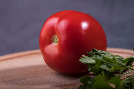 Juicy red tomato with a sprig of parsley close-up on the table.の写真素材
