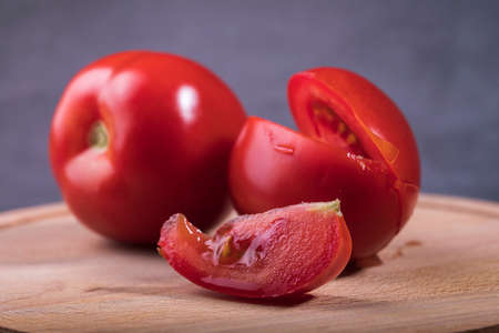 There are red tomatoes on the table and a slice is cut off from the tomato.の写真素材