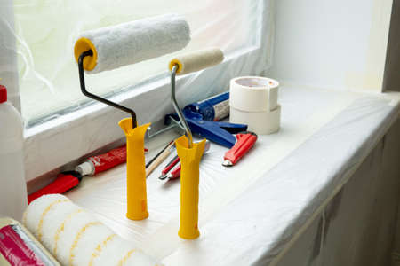 Two paint rollers and paint pan with gray paint in room near wall, painting works. Renovation and construction works at room in flat, apartment, house. Prepared tools for work.の写真素材