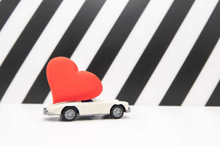 White retro toy car delivering a heart on a black and white background. Postcard February 14, Valentine's Day. Flower delivery. March 8, International Happy Women'sの写真素材