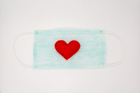 Disposable medical mask on blue background with red heart on it against bacteria and viruses. Stop the spread of coronavirus, self-defense.の写真素材