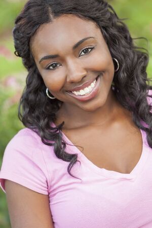 A beautiful happy young African American woman or girl relaxing and smiling outsideの写真素材