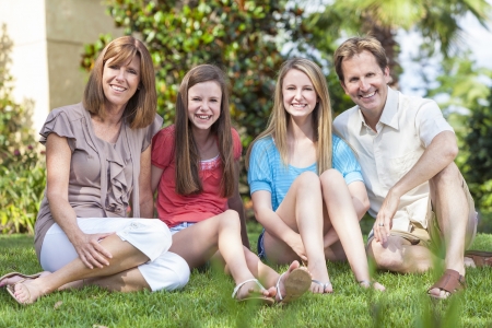 An attractive happy, smiling family of mother, father and two daughters sitting together outside in...