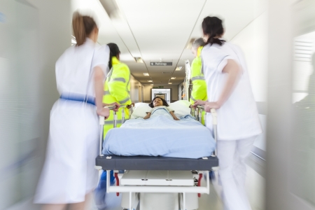 A motion blurred photograph of a young Asian Indian girl child patient on stretcher or gurney being pushed at speed through a hospital corridor by doctors & nurses to an emergency roomの写真素材