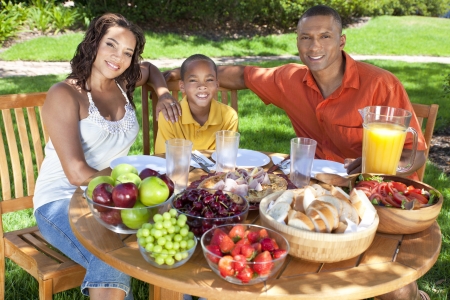 A happy, smiling African American family, mother father & son eating healthy food at a table outside, the father is serving a orange juice to the boy.の写真素材