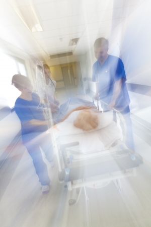 A motion blurred photograph of a senior female patient on stretcher or gurney being pushed at speed through a hospital corridor by doctors & nurses to an emergency roomの写真素材