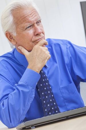 A senior man male businessman sitting at a desk wearing a shirt and tue using a computerの写真素材