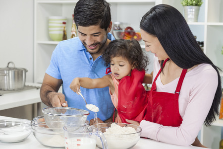 Asian Chinese family, man & woman parents and young girl child daughter cooking, baking, making cakes in home kitchenの写真素材