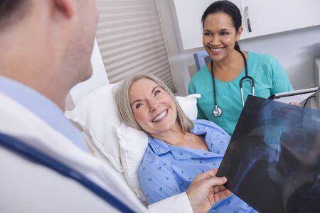 A happy senior female woman elderly patient in bed looking at X-ray with male doctor and Hispanic...