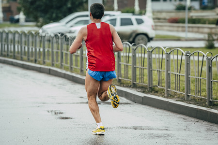 man athlete running on the wet road, their feet on the dirt